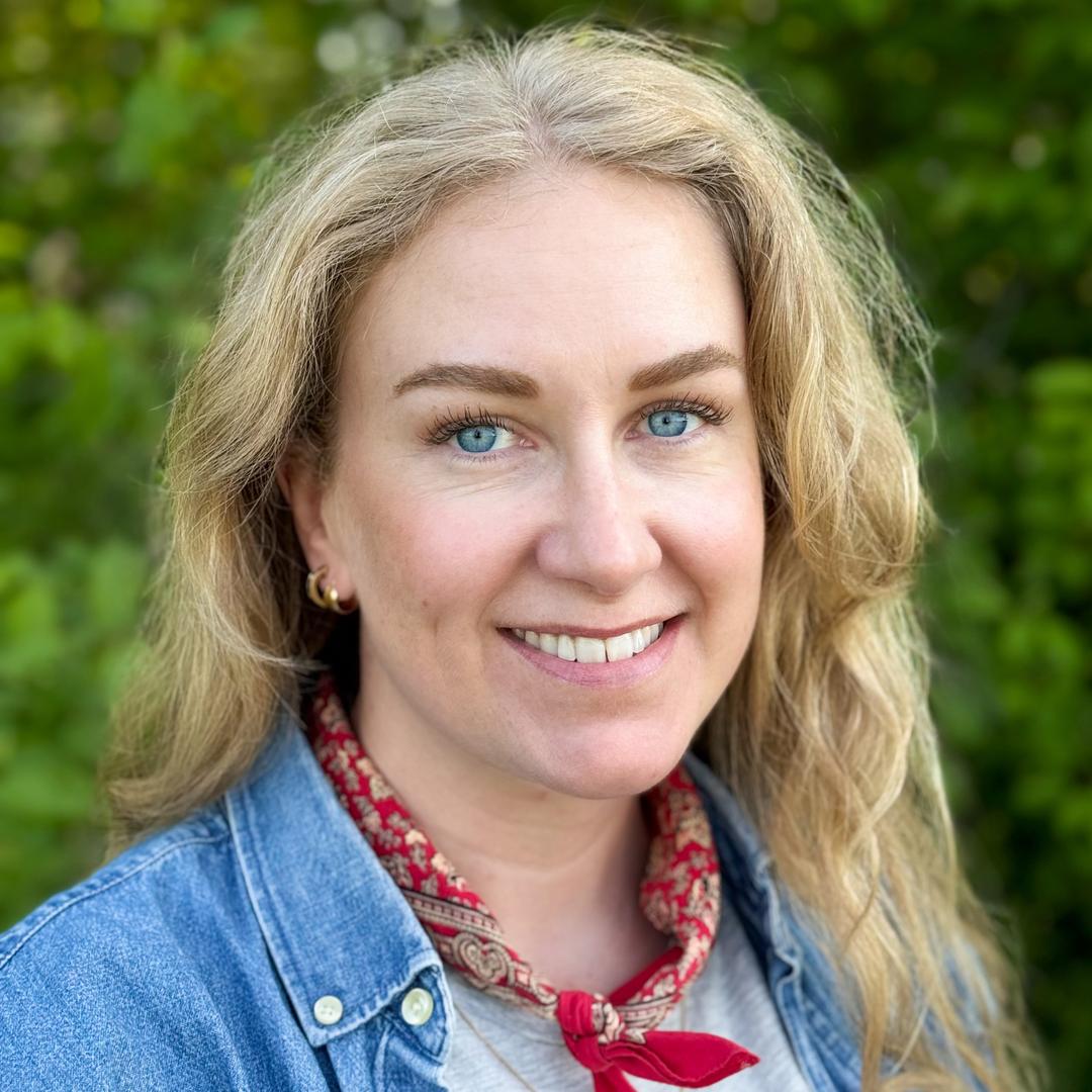A woman with long, blond hair, wearing a denim shirt, looks into the camera.