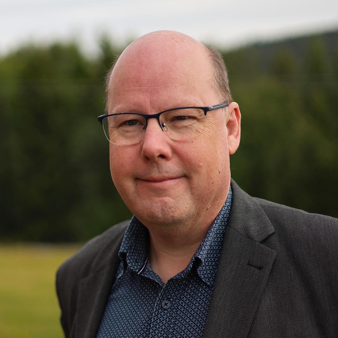 A man with glasses, wearing a jacket, looks into the camera.