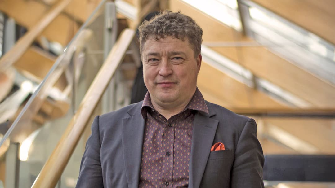 A man in a jacket looks into the camera. 
