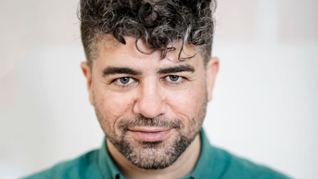 Man with a green shirt looks straight at the camera.