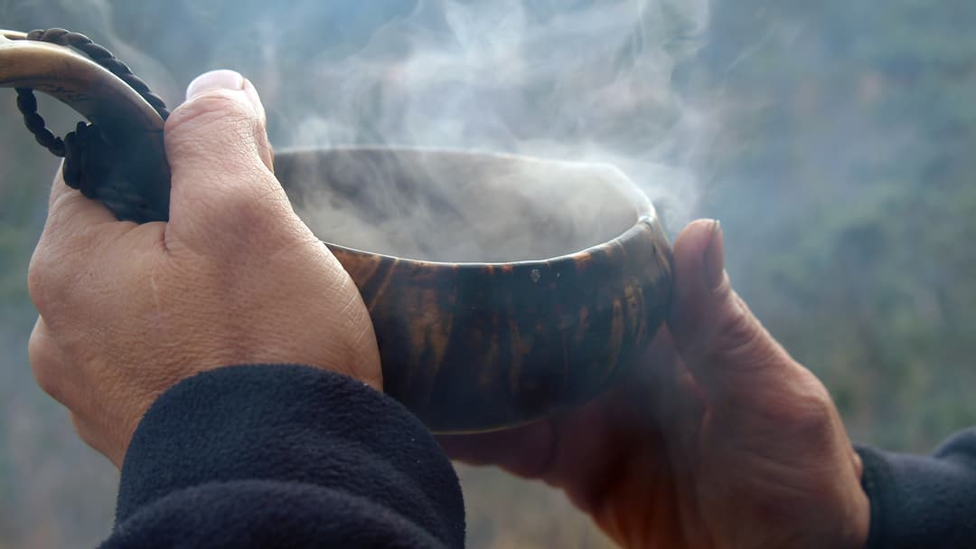 Två händer som håller en guksie, kåsa, med rykande kaffe. 