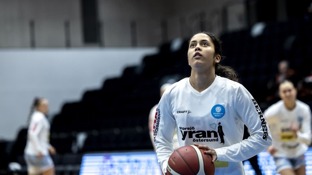 Ung kvinna ska till att skjuta en basketboll mot korgen.