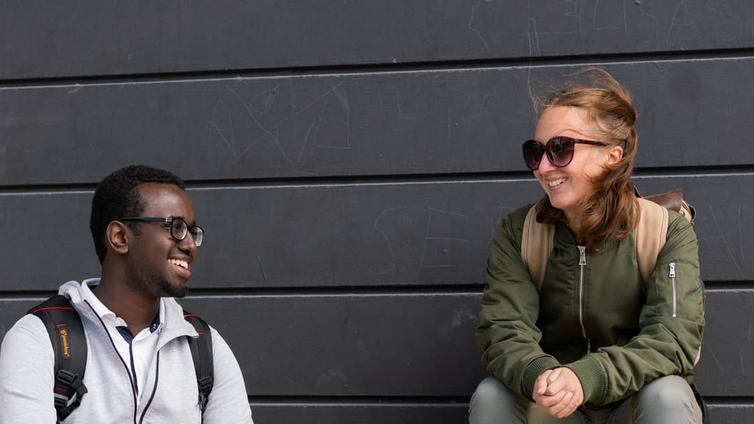 Två studenter som sitter på gul bänk. 