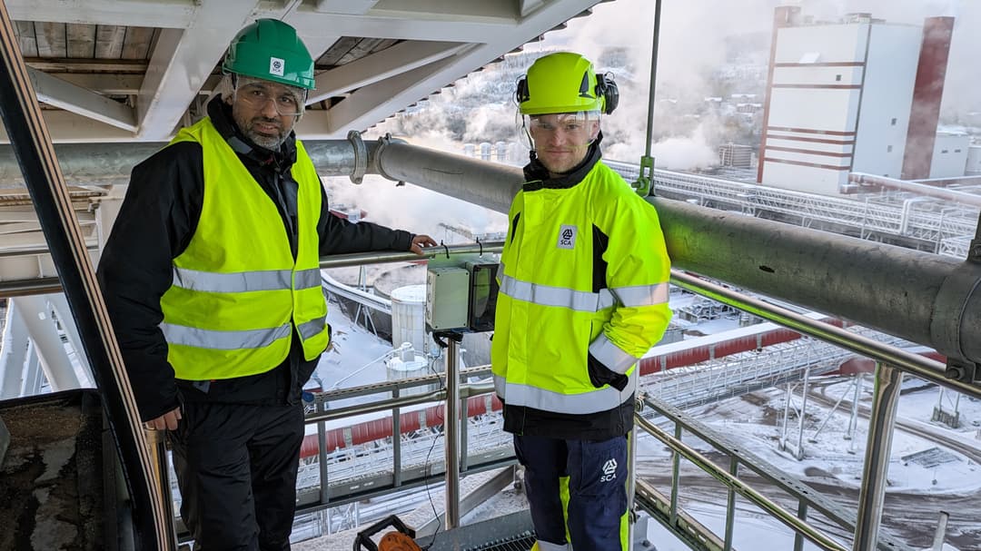Två män i varselkläder i ett vintrigt industrilandskap.