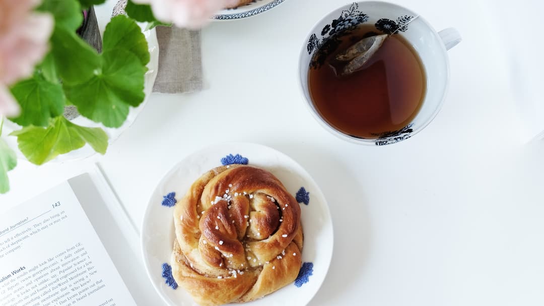 En kopp te och bulle på ett vitt bord med blomma i förgrunden