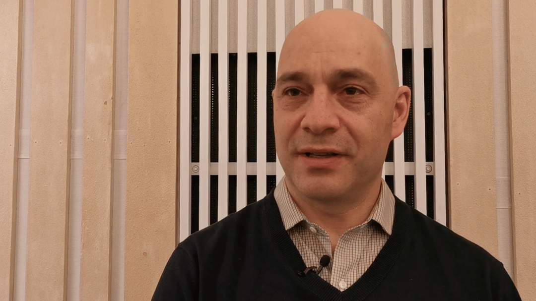 Man with shirt and black sweater being interviewed