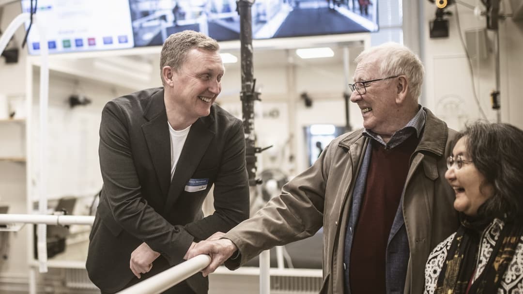 Man står lutandes mot staket och ler mot glad kvinna och glad man i ett forskningslabb. 