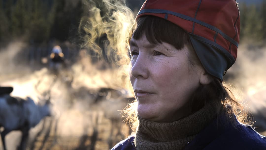 Kvinna i sydsamisk kvinnomössa andas så det bildas imma runt henne.