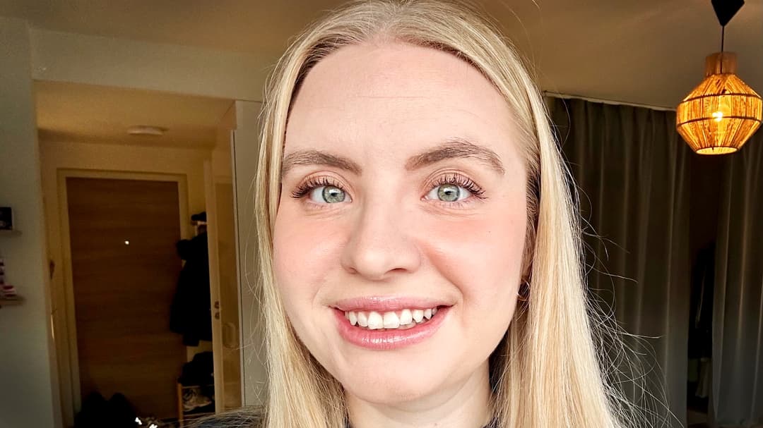 Kvinna med långt blont hår ler in i kameran.