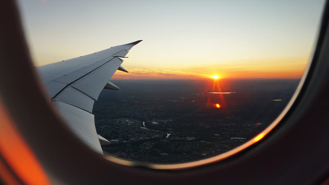 Flygplansvinge och solnedgång genom ett flygplansfönster