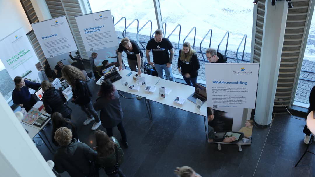 Studenter som står bakom ett bord och visar Mittuniversitetets utbildningar. 