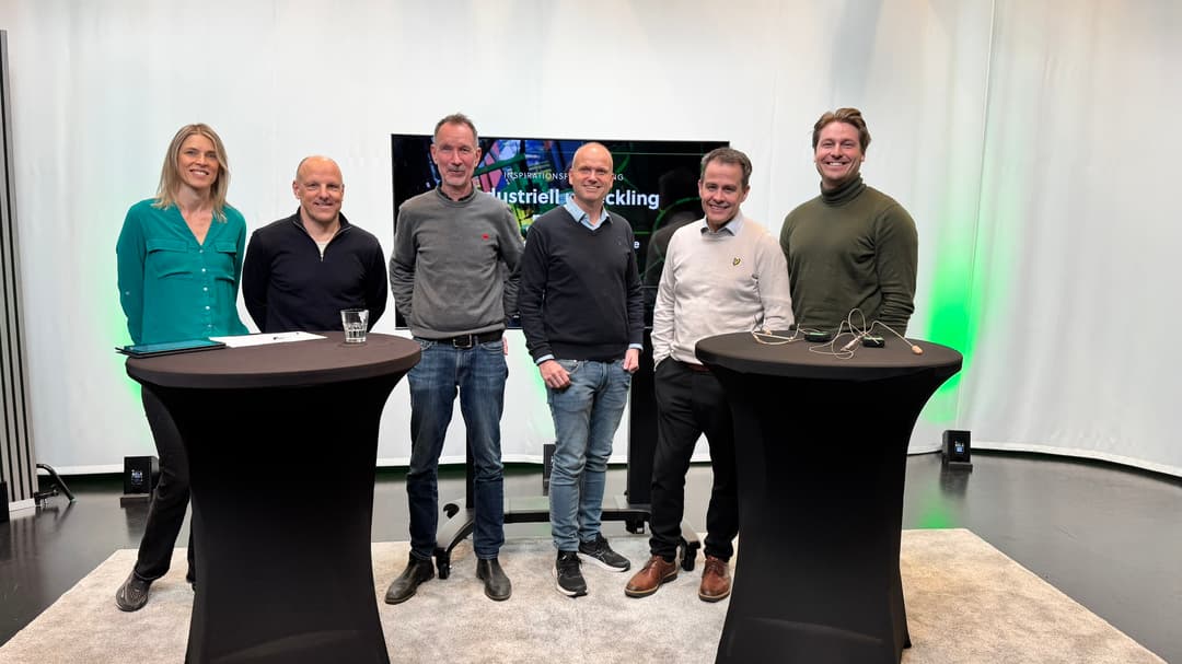 6 persons standing behind 2 tables and smiles at the camera