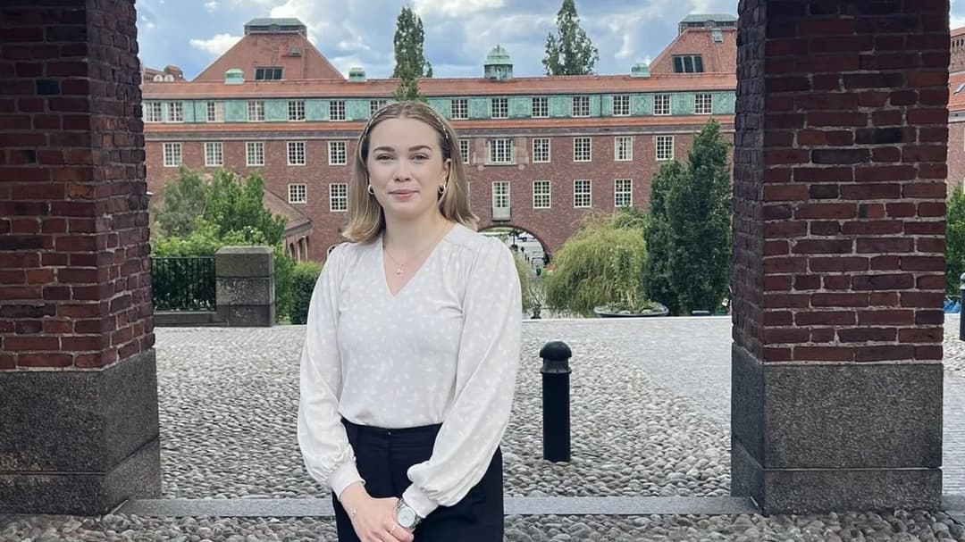 En kvinna med vit tröja och svarta byxor framför en byggnad