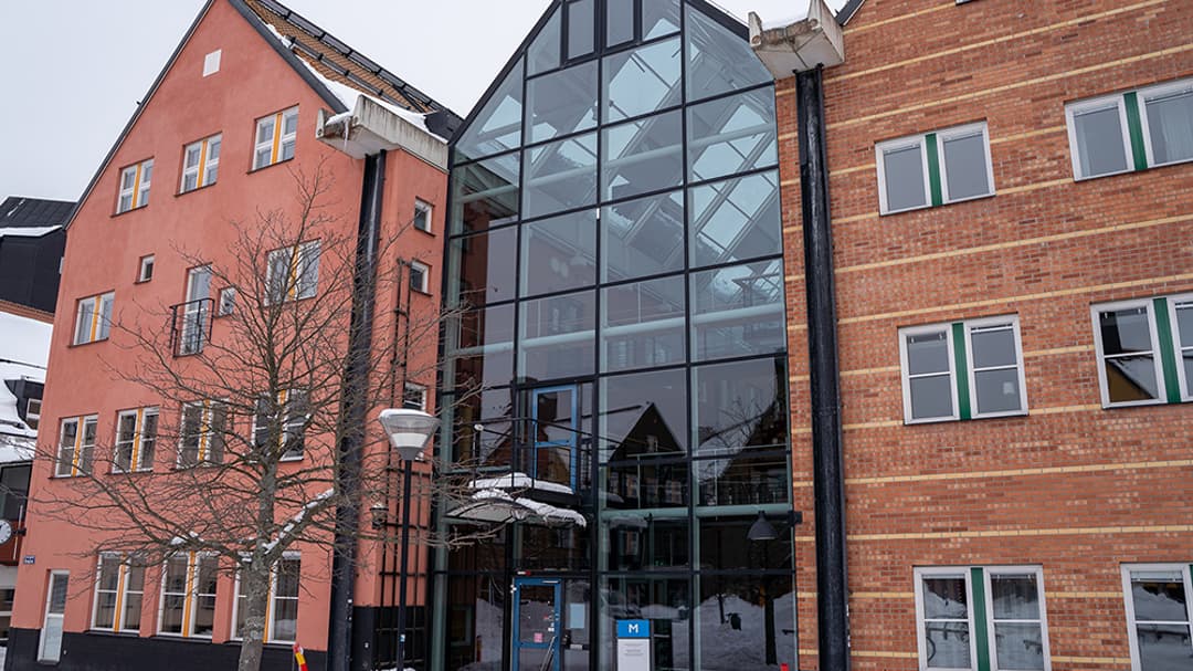 Röda byggnader ihoplänkade med en glasbyggnad.