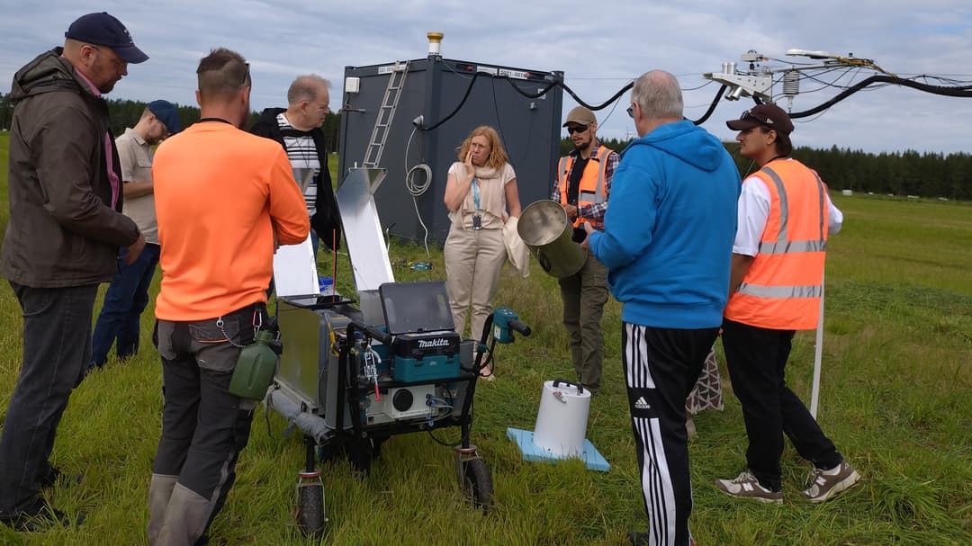 Several people are standing on a grassy field and looking at measuring equipment.