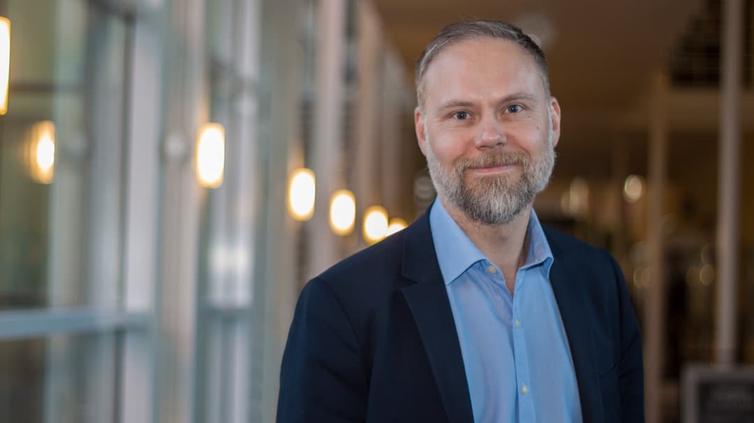 Man med skägg iklädd mörk kavaj och ljusblå skjorta