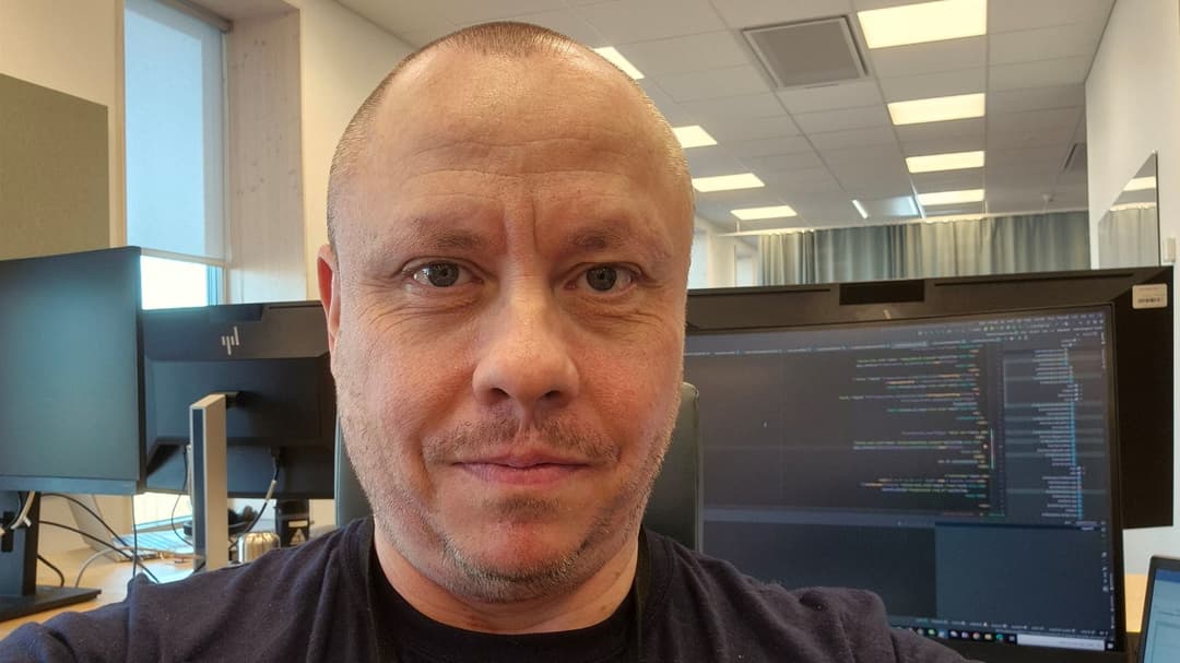 En man sitter i ett kontorslandskap med en datorskärm bakom sig.