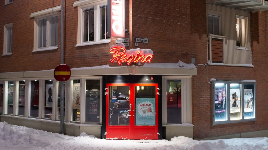 Skyltfönstret och entren till en liten biograf i Östersund. Den har röd entredörr och ovanför dörren sitter en neonskylt som visar biografens namn Bio Regina