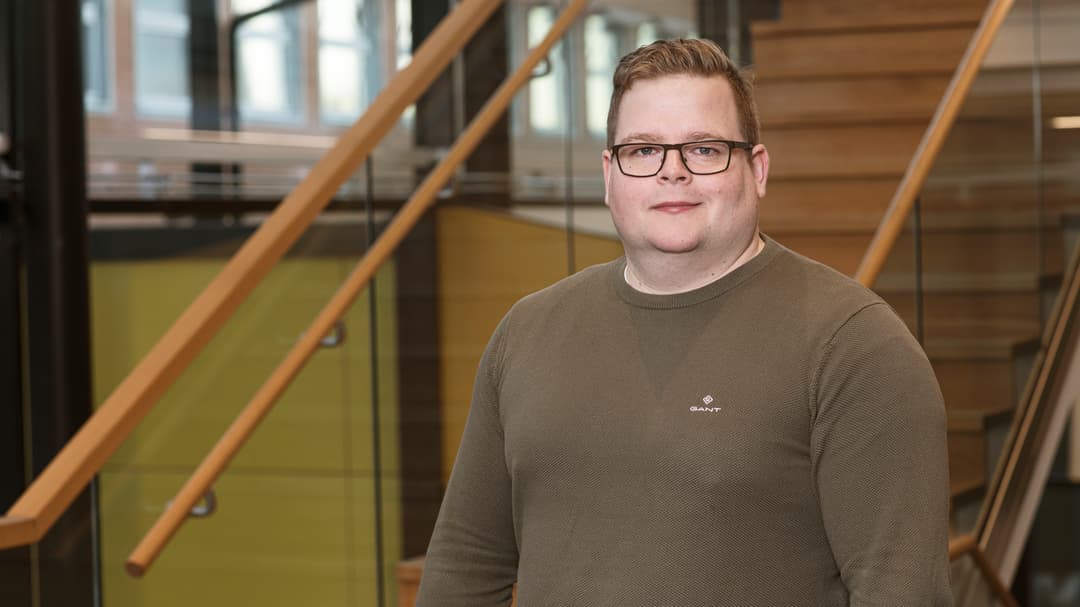 En man med glasögon och brun tröja ler mot kameran
