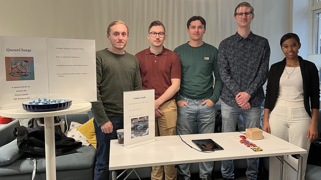 Fem personer står bakom ett bord där en prototyp på ett virtuellt kösystem för elbilsladdare ligger.