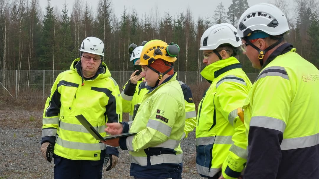 En grupp män i varselkläder står tillsammans och tittar på en bärbar dator. 