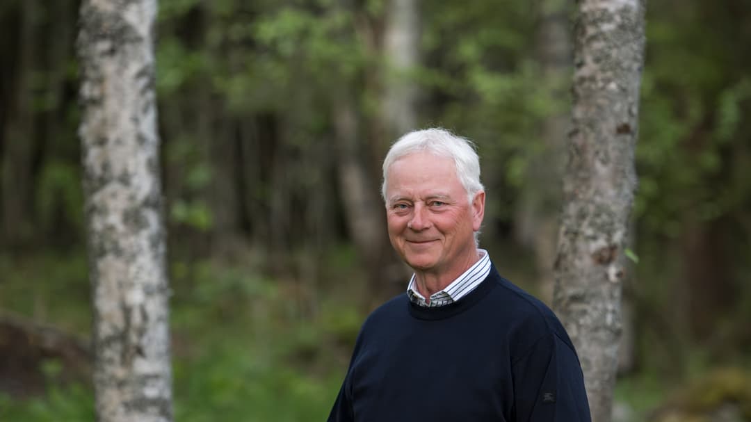En man i mörk tröja står i en skog.