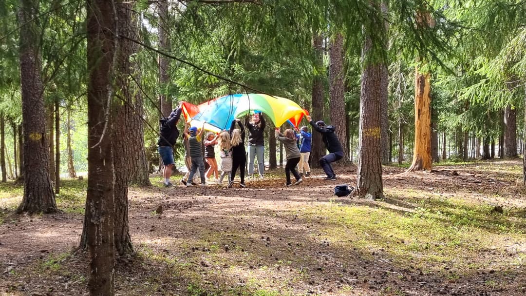 flera barn som håller upp ett färgglatt segel i skogen