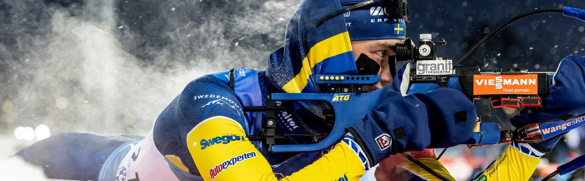 Skidskytt som ligger och siktar med sitt gevär, det ångar från ryggen.