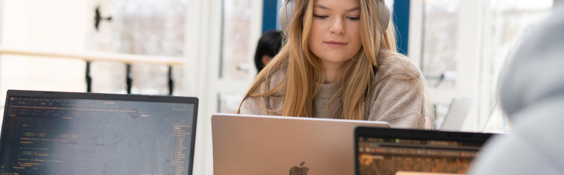 En kvinna med hörlurar sitter vid en laptop
