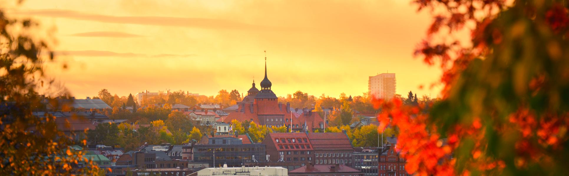 View of Östersund City Hall against a sunny yellow sky, with trees in autumn colors visible in the foreground.