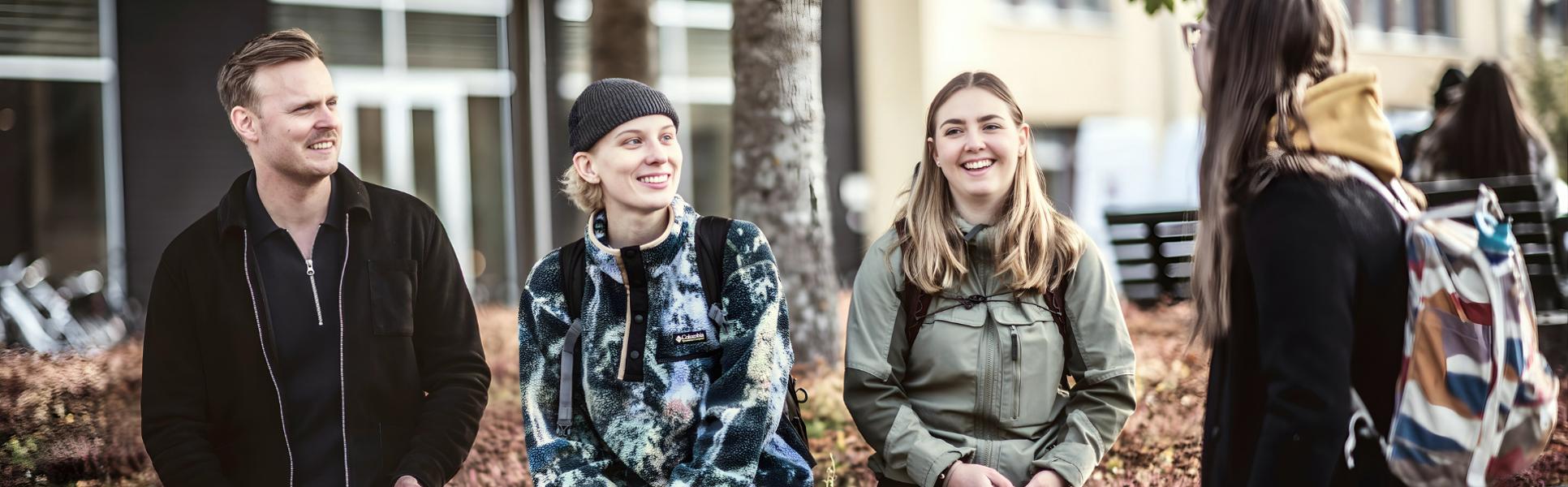 Fyra studenter sitter utomhus på campus i Östersund, de ser glada ut glada och pratar med varandra 