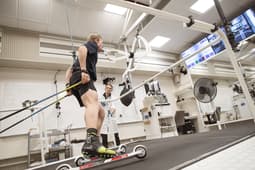 Alfred Buskqvist åker rullskidor på rullband med testutrustning som mäter syreupptagning, övervakas av testledare Hampus Lindblom.