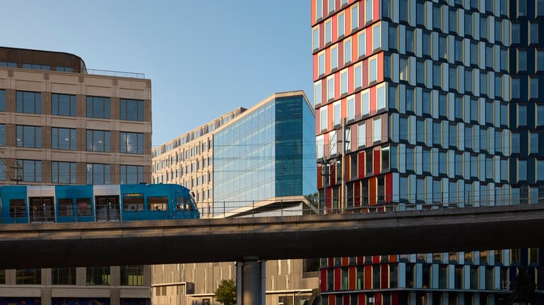 Stadsbild med höga hus och tåg på upphöjd räls i förgrunden.