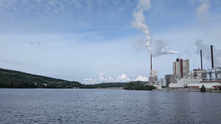 Fabrik med bolmande rök invid vatten
