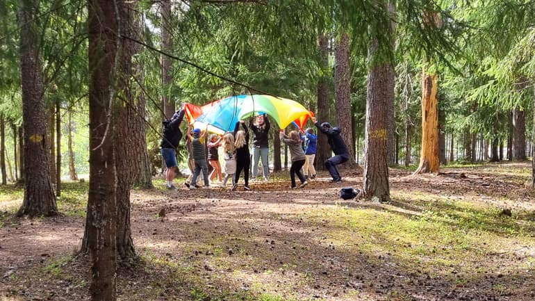 flera barn som håller upp ett färgglatt segel i skogen