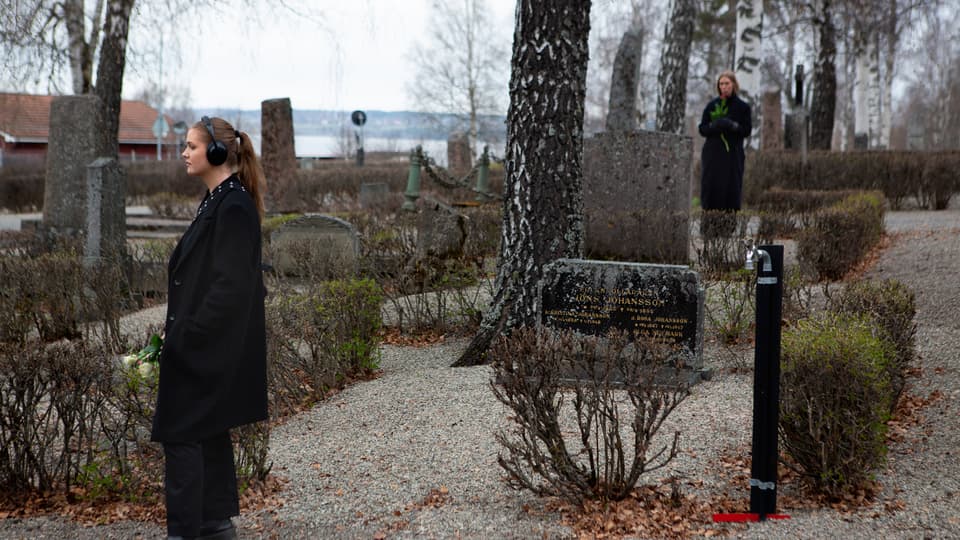 Två svartklädda personer med hörlurar vandrar på en kyrkogård.