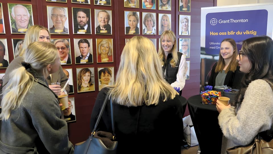 Studenter och företagsrepresentanter minglar framför en vägg prydd av många tavlor.