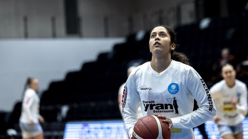 Ung kvinna ska till att skjuta en basketboll mot korgen.