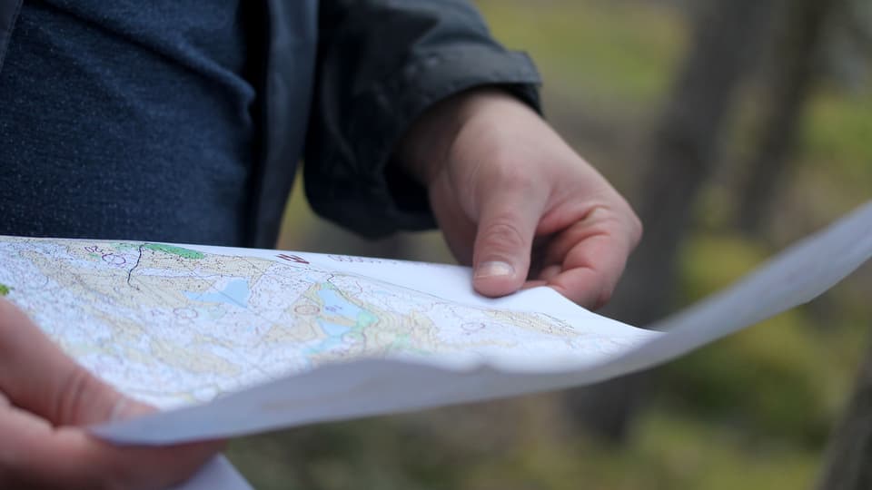 Person läser orienteringskarta med natur i bakgrunden