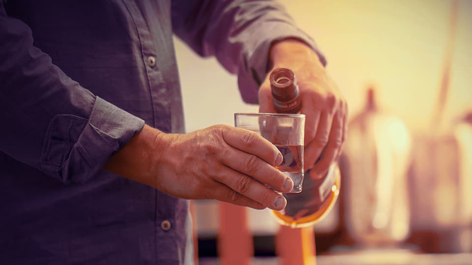 Elderly man pouring alcohol into a glass.