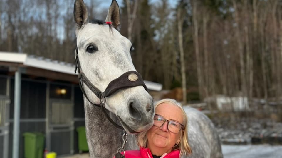 En kvinna står utomhus med en häst vid sin sida.