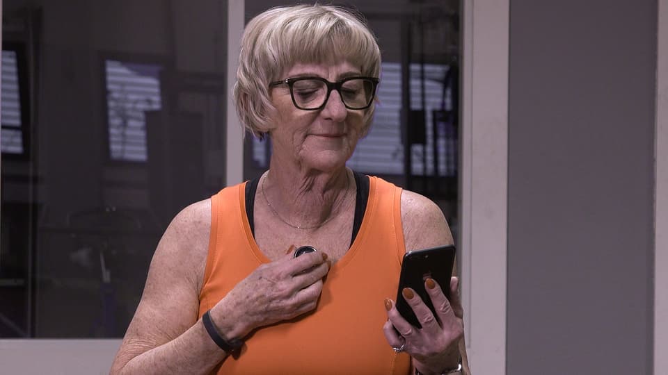 Kvinna på gym spelar in ljud från sitt hjärta via mobilen. 