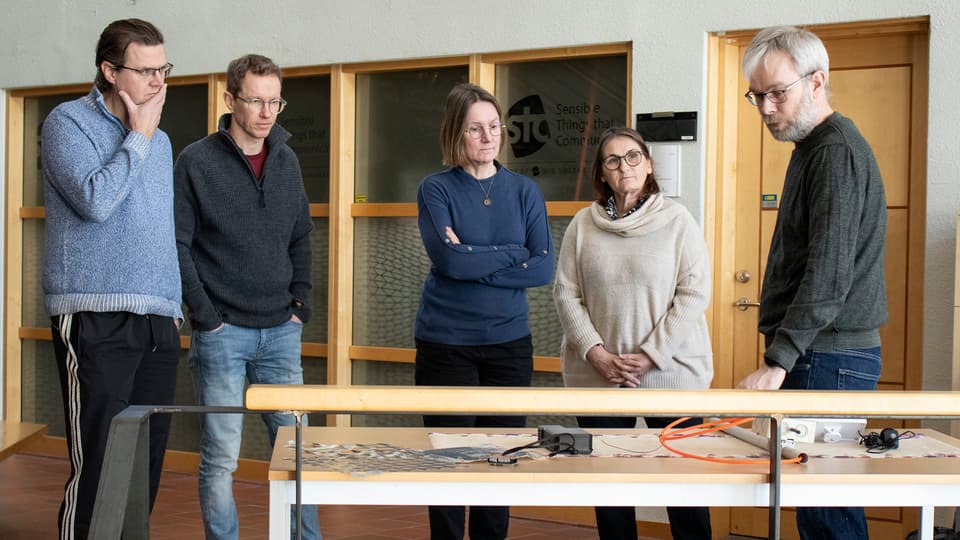 Four people stand and listen to a man who talks about various prototypes produced in research projects.