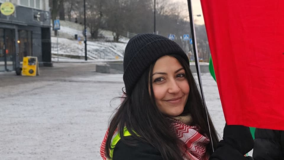 Foto av en kvinna som står utomhus vid ett rött tygstycke.