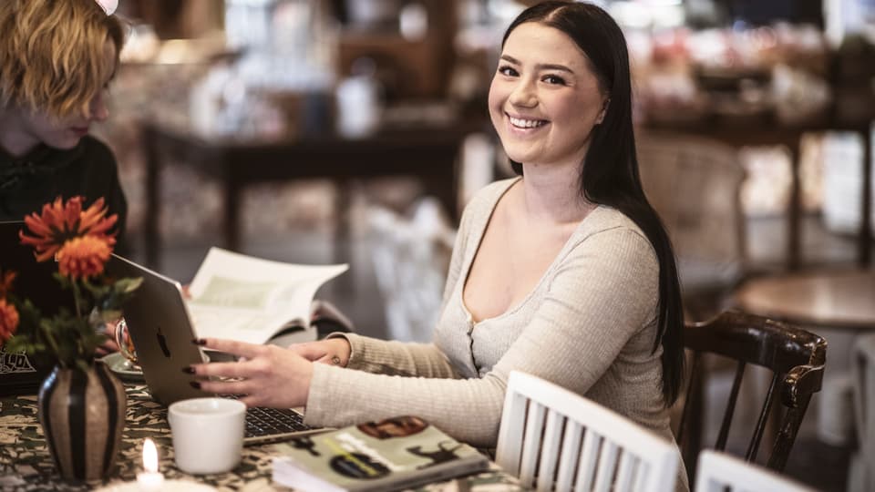 A woman is smiling at the camera. She is sitting by a computer.