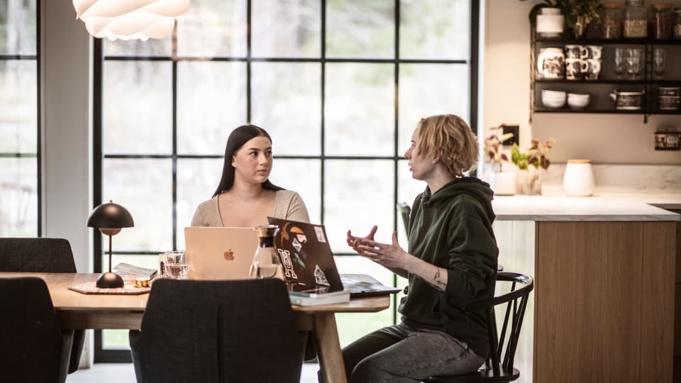Two women sitting at a kitchen table working at their computers. 