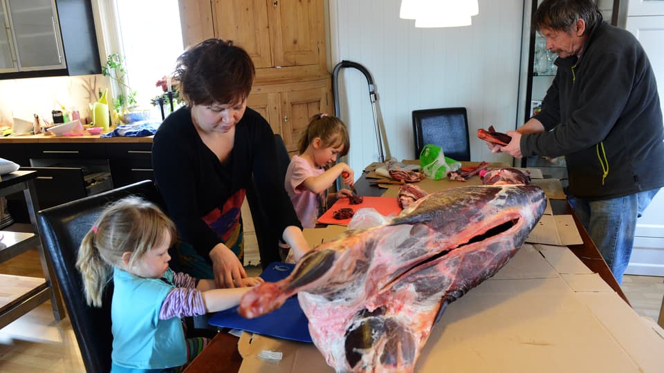 Kvinna, man och två barn styckar en renkropp på köksbordet.