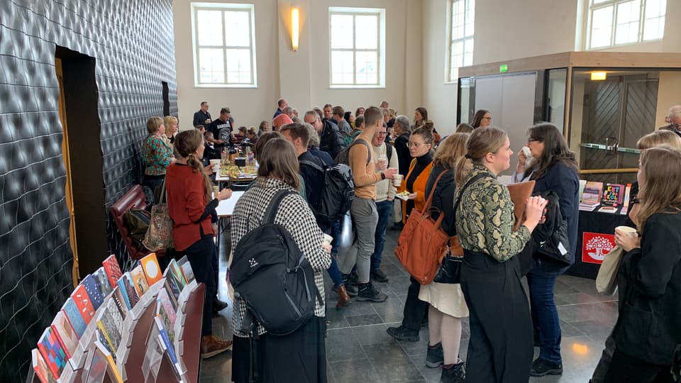 Människor fikar i en lobby med bokbord.