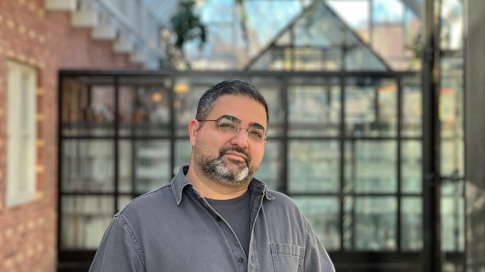 A man stands in a courtyard, he looks into the camera.