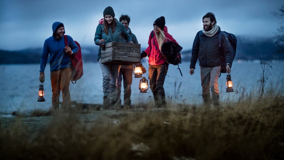 Five people walk with lanterns by the beach at he High Coast in Sweden